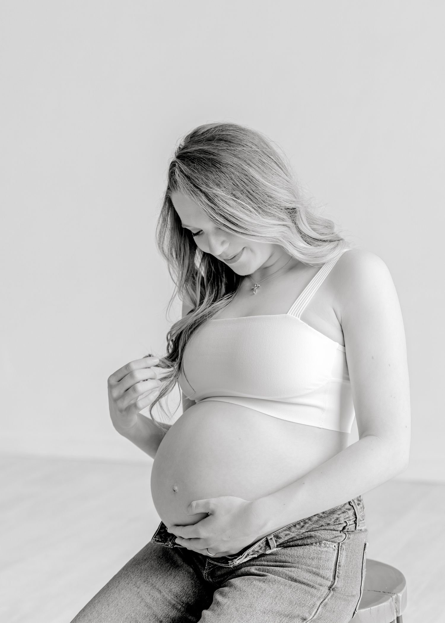 Black and white maternity photo showing pregnant woman in white top and jeans looking down at baby bump.