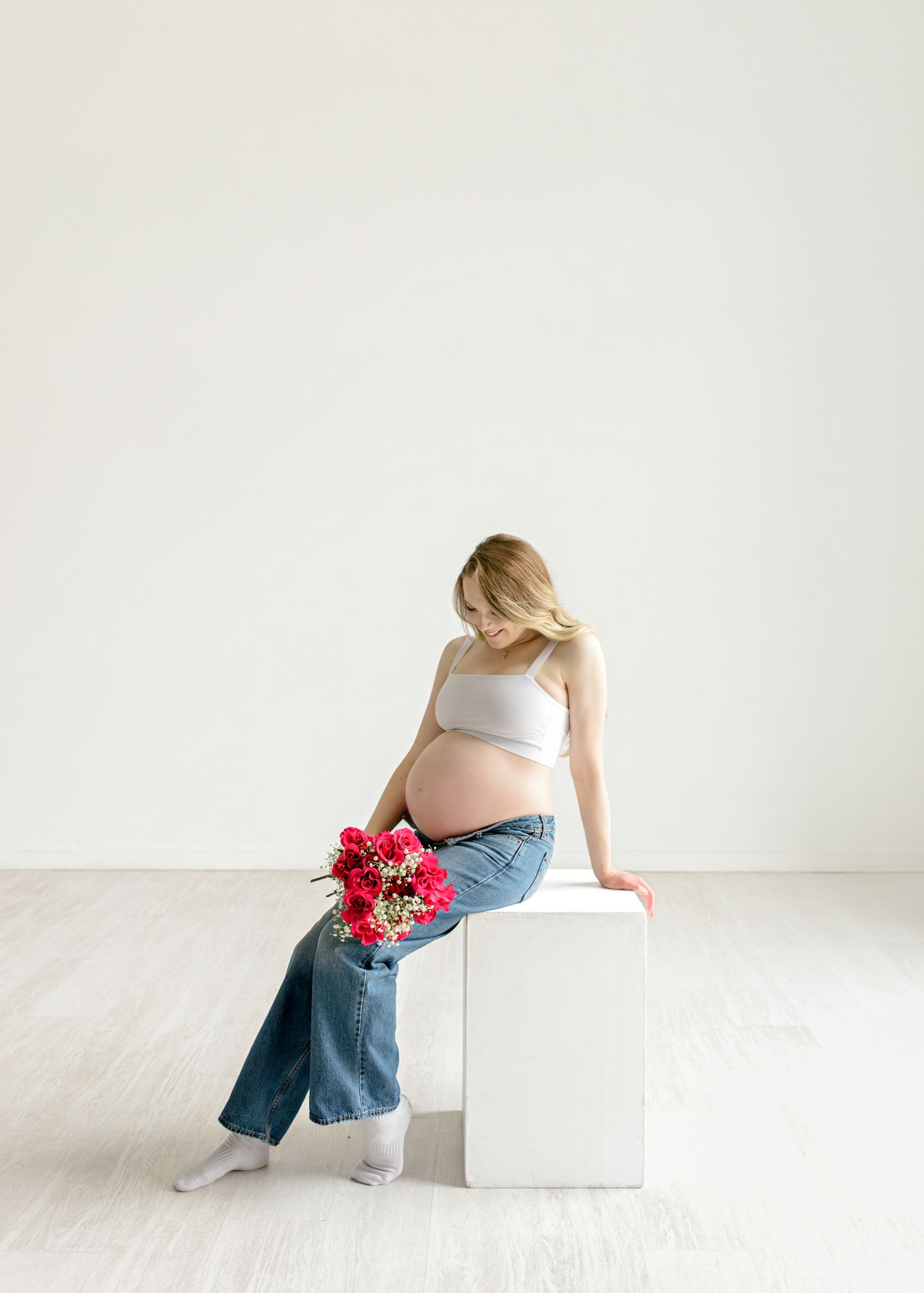 A series of studio images showing someone wearing jeans and a white top sitting on a white platform with pink flowers.