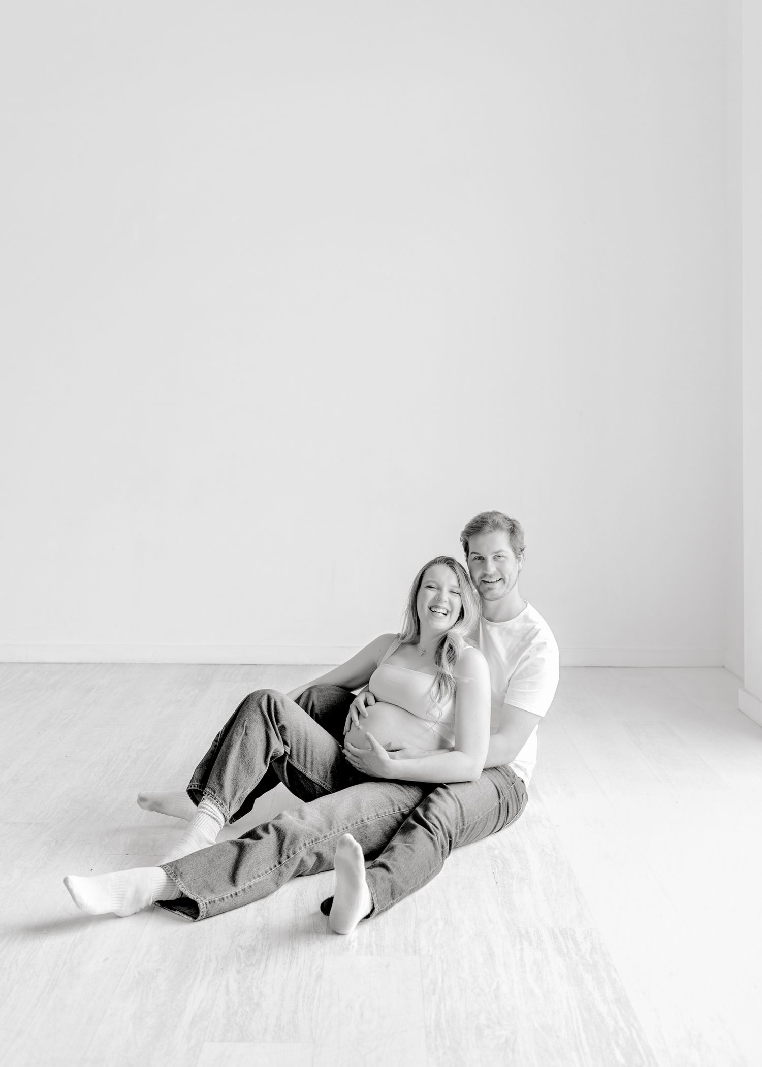 Couple in casual white clothing sitting together on floor in minimalist black and white photo.