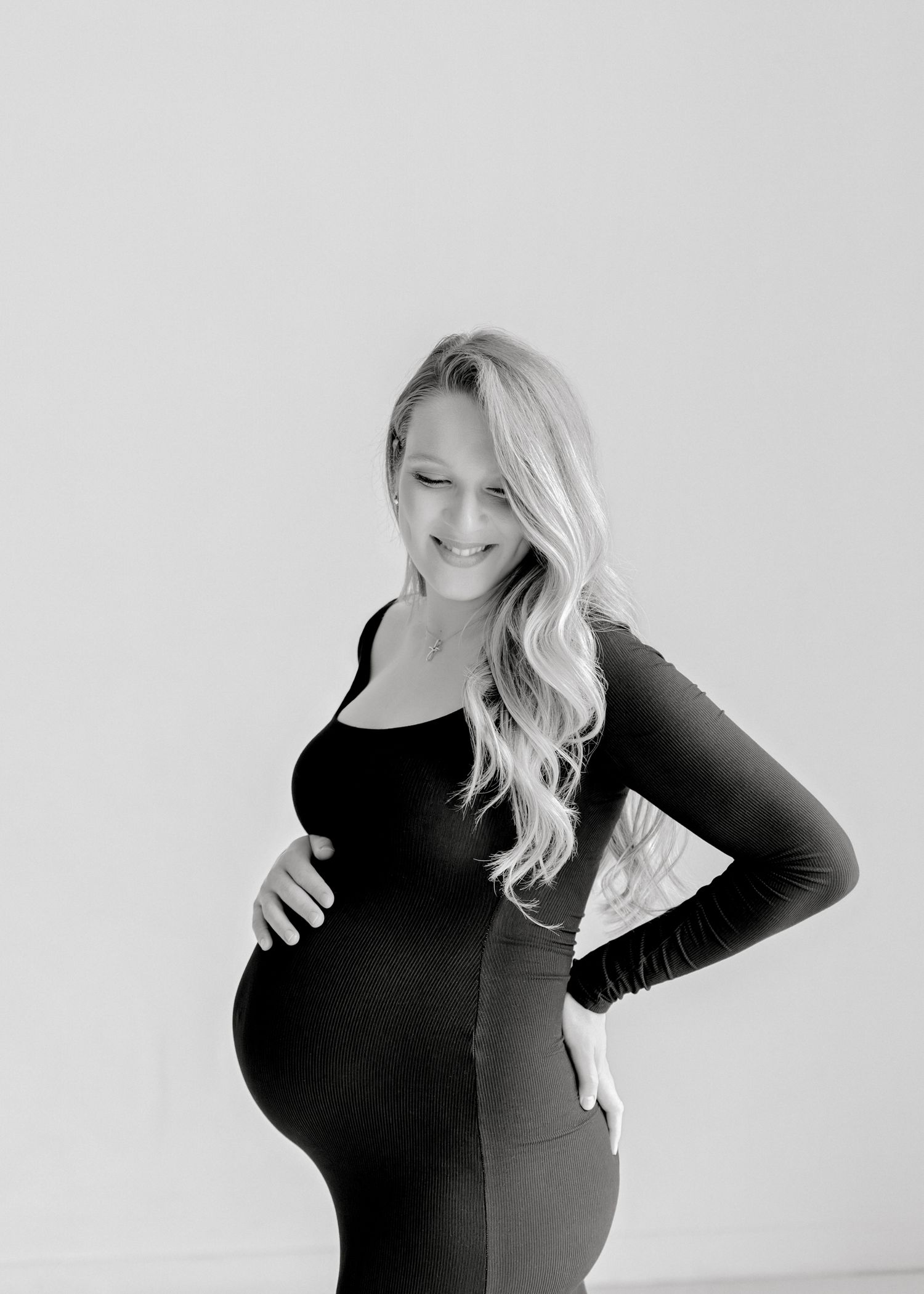 Black and white portrait of an expectant mother in a long sleeve top posing against a light background.