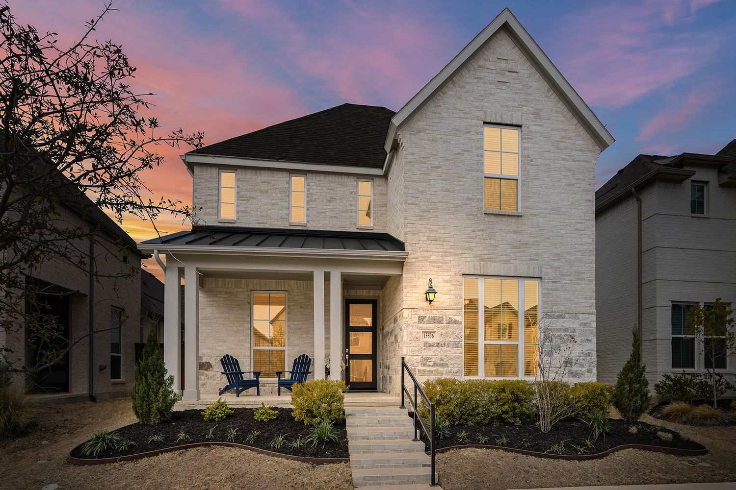 Modern white farmhouse-style homes with illuminated windows glowing warmly at sunset against a pink and purple sky.