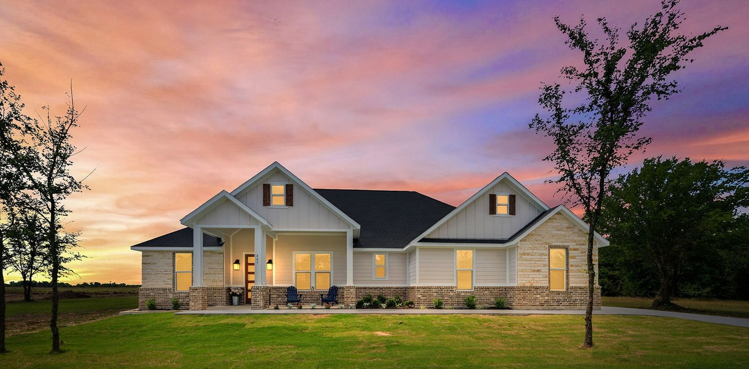 Elegant ranch-style home with illuminated porch and warm exterior lighting set against a vibrant sunset sky.