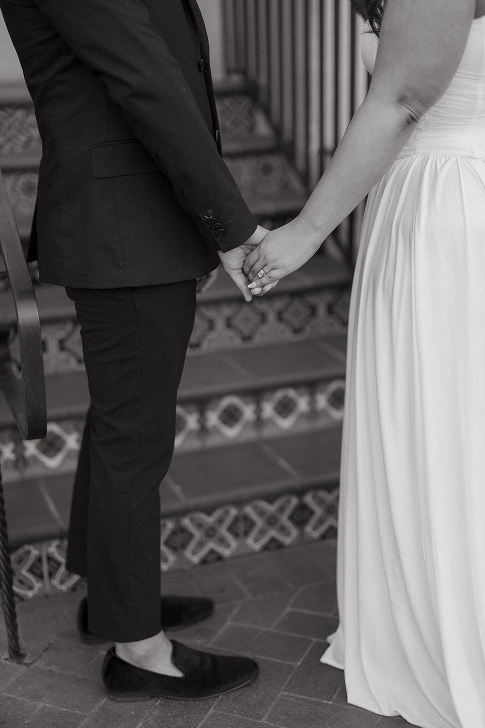 Close-up view of formal wedding couple on ornate tiled staircase showcasing dress and suit details.