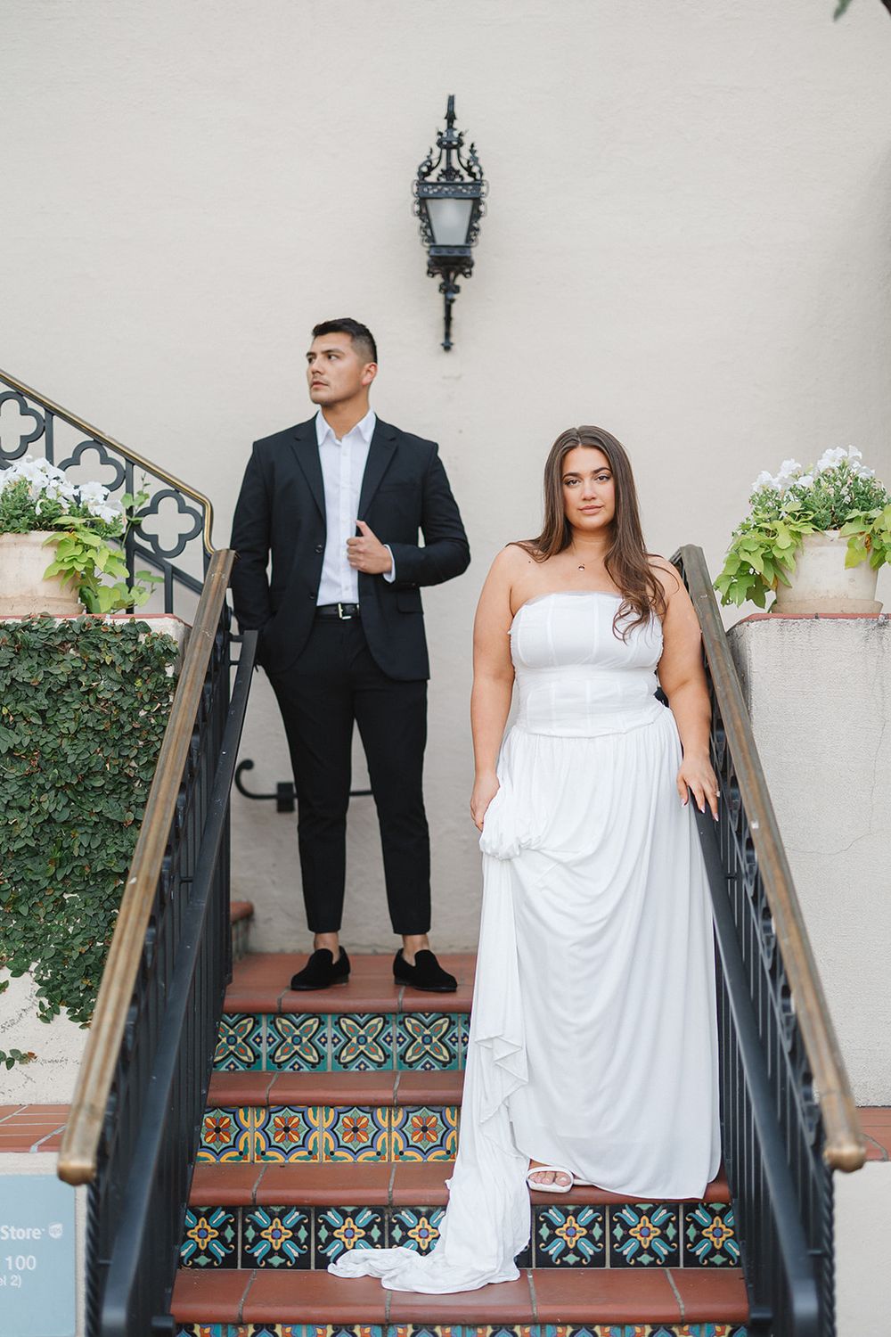 A couple poses on decorative tiled steps in formal wedding attire with white dress and black suit.