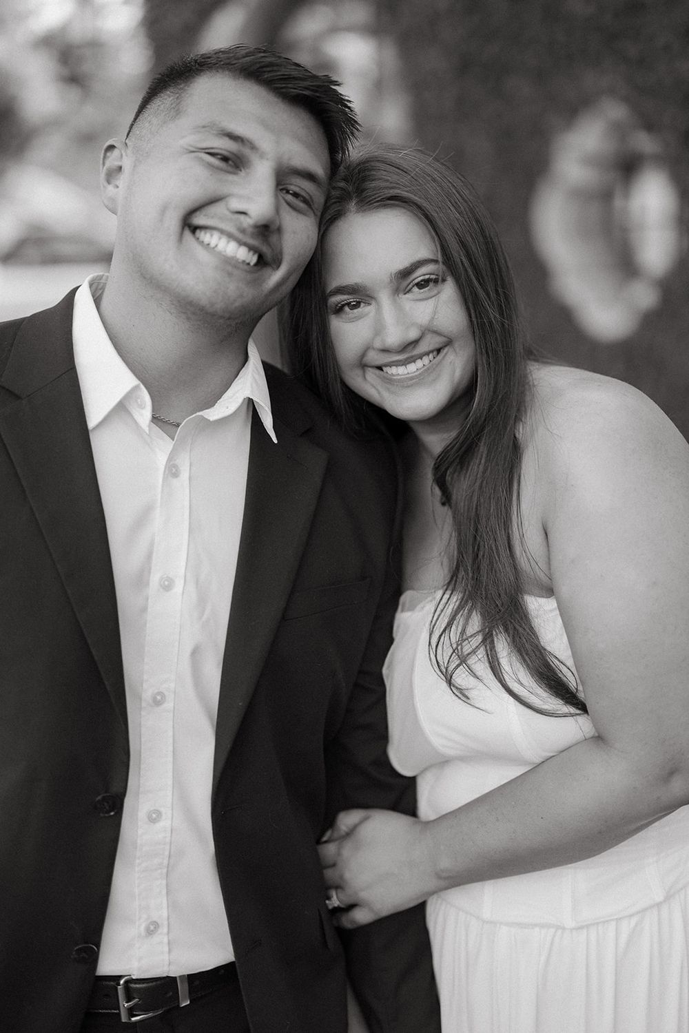 A romantic black and white portrait of a couple in formal attire smiling together outdoors.