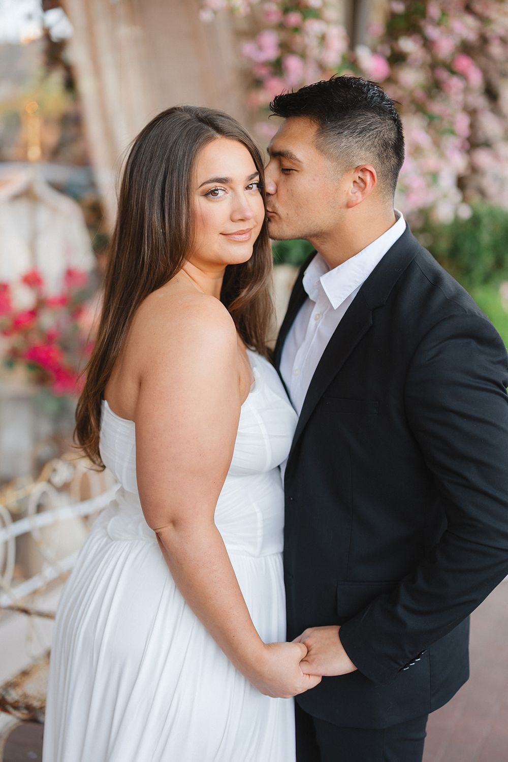 A tender moment between a couple in wedding attire posing against a backdrop of pink floral blossoms.