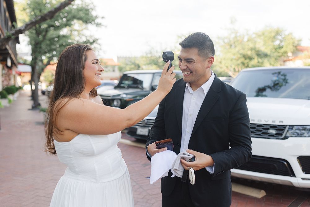 A couple sharing a lighthearted moment while standing on a brick sidewalk next to parked cars.