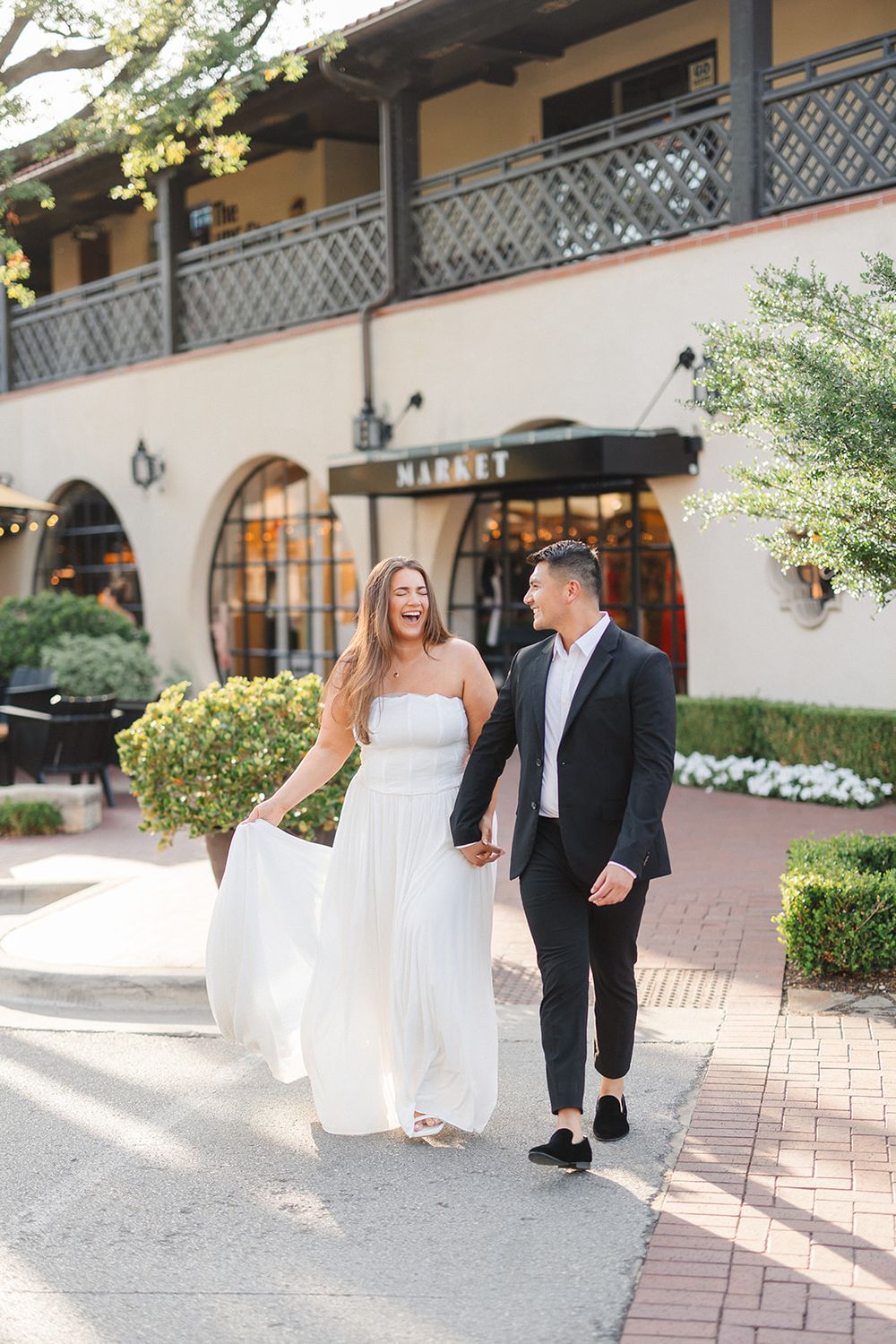 A couple walking together along a Spanish colonial style building with ornate balconies and storefronts on a sunny day.