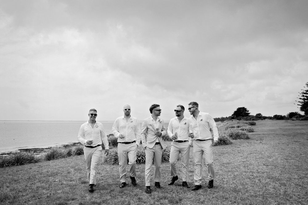Men in light colored suits walk in a field under a moody sky.