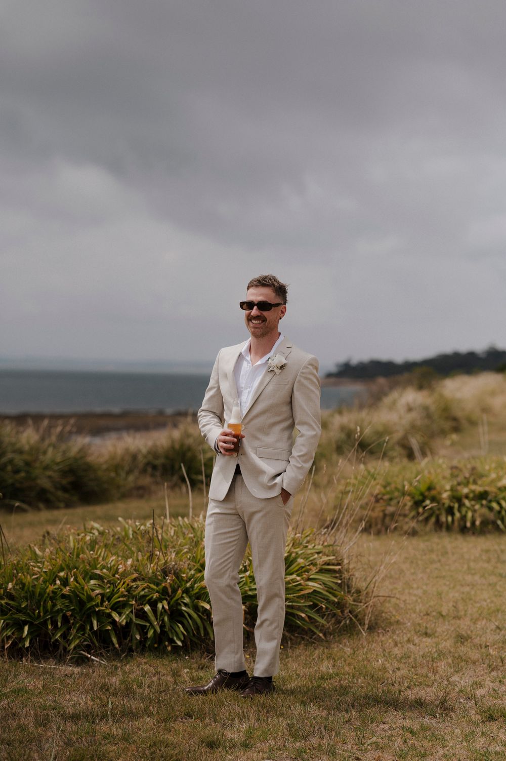 Person in a light suit stands alone in a grassy coastal field.