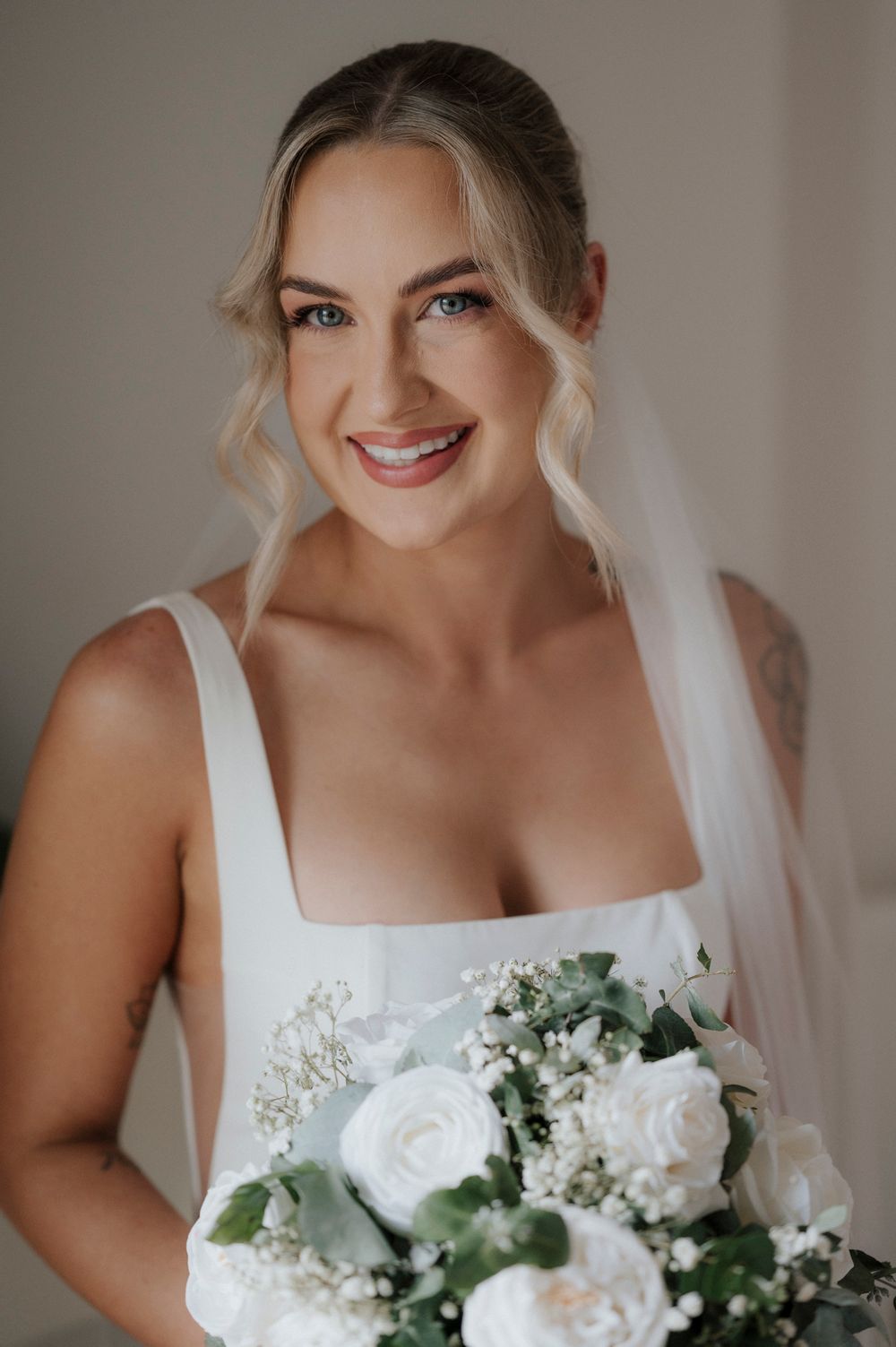 White wedding bouquet with roses and greenery against an elegant bridal gown.