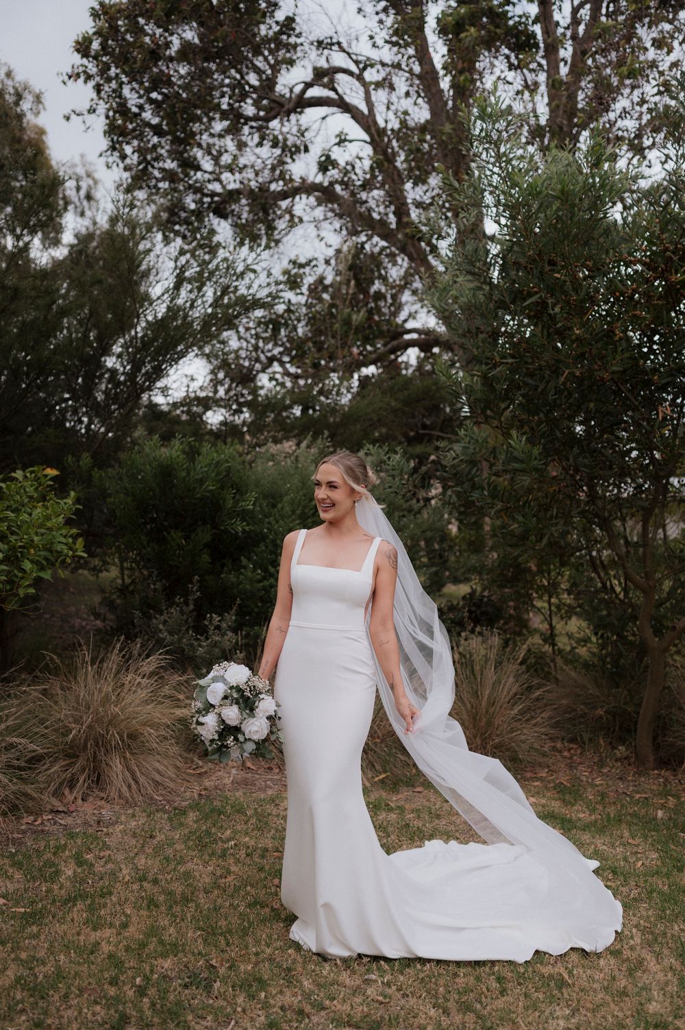 Classic white wedding gown with train flowing in an outdoor garden setting.