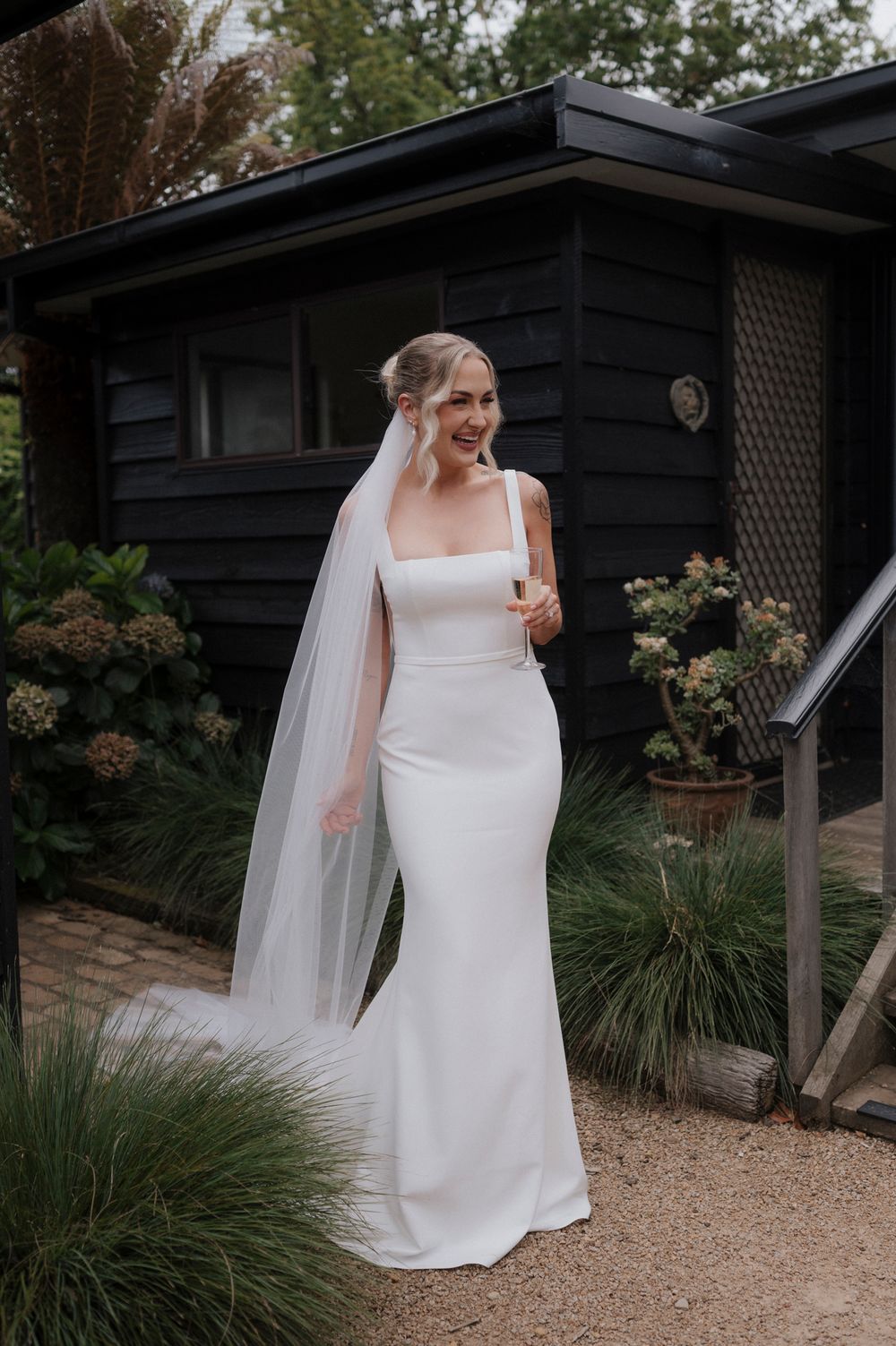 Elegant bride in white dress poses near black building exterior.