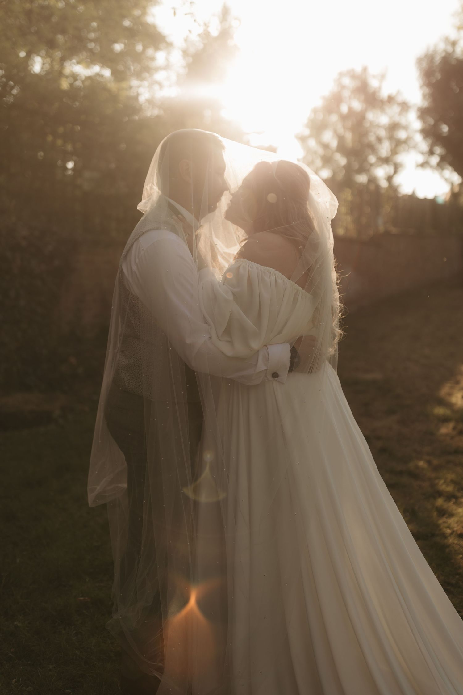 A couple holds hands in a dreamy outdoor wedding photo with tall golden grass and soft sunlight.