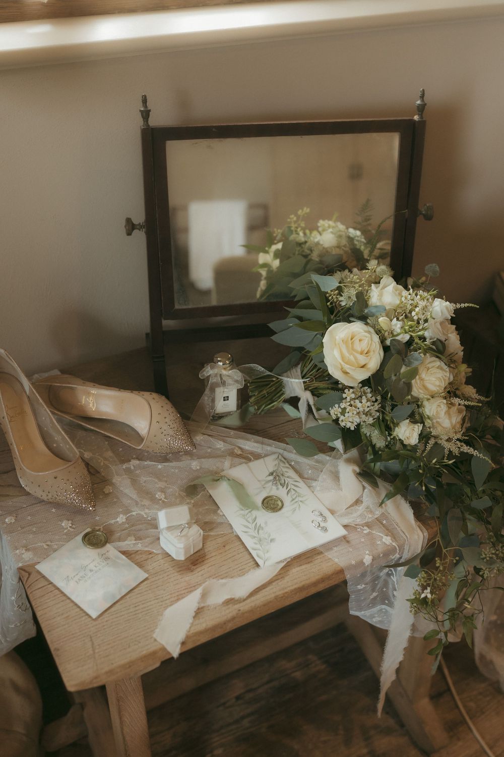 Elegant white roses and floral arrangements rest beside wedding invitations on a rustic wooden bench.