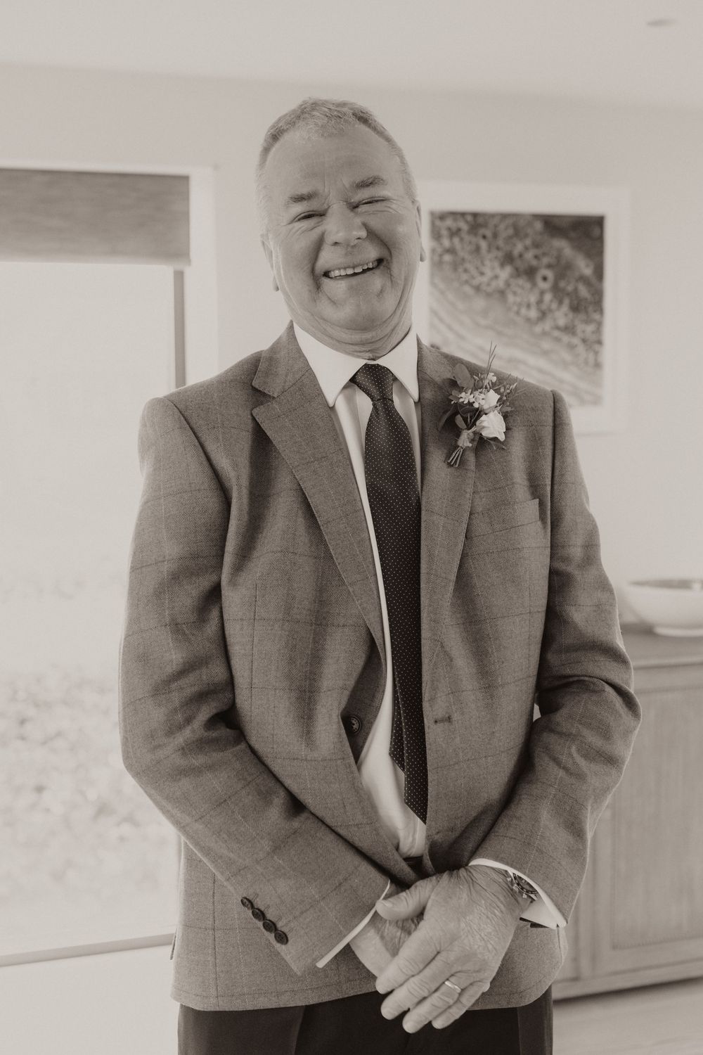 Man in formal suit with boutonniere smiling warmly in black and white portrait.