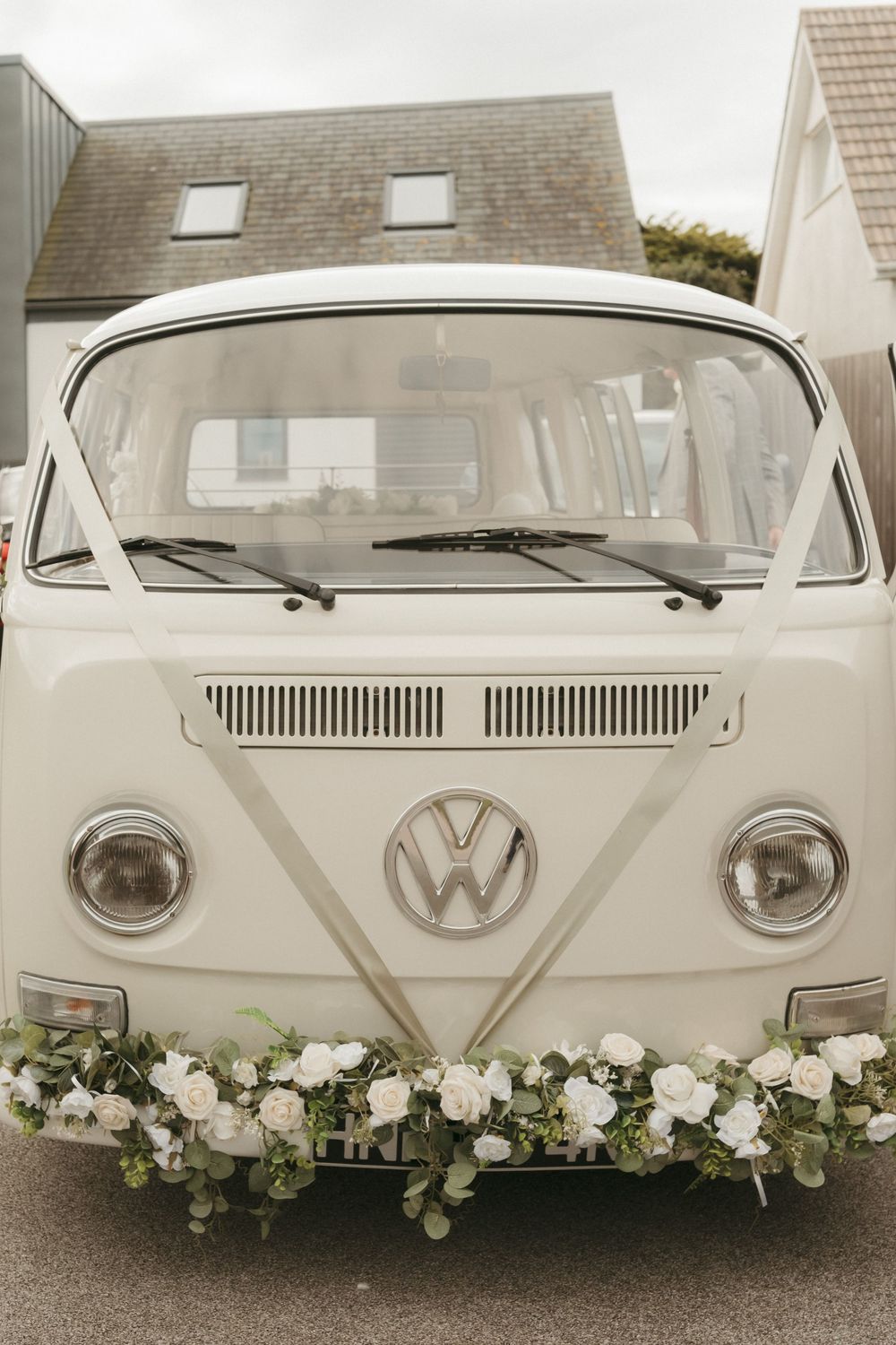 Classic white Volkswagen van decorated with elegant floral arrangements along its front grille for a wedding.
