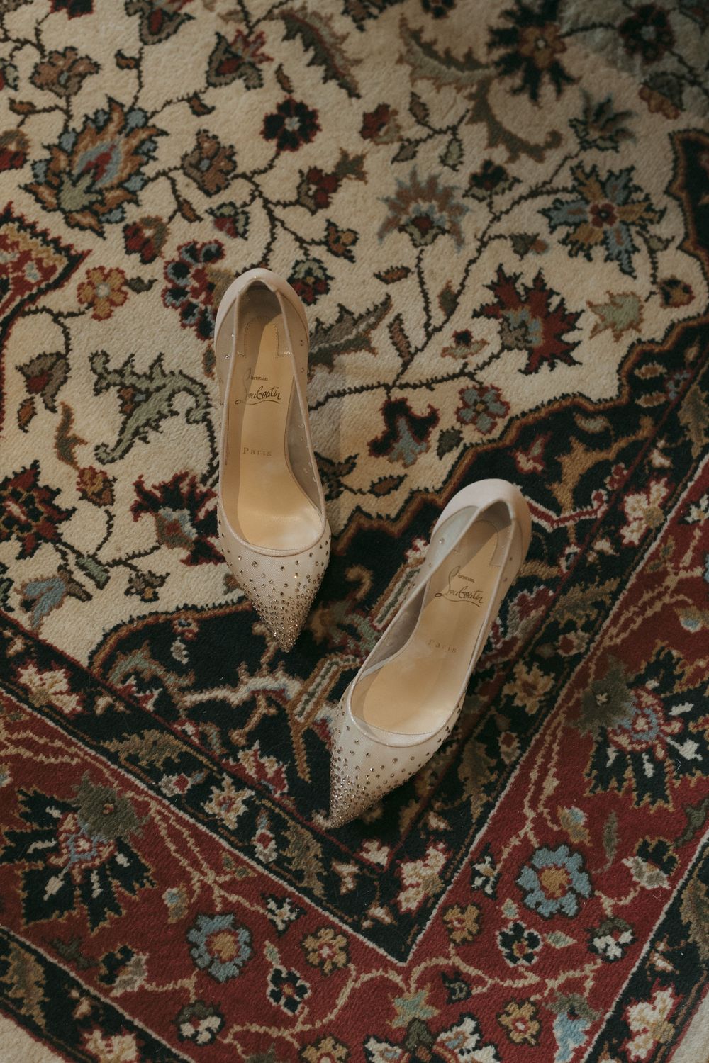 Sparkly silver wedding heels displayed on an ornate floral patterned oriental rug.