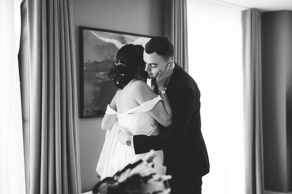 A black and white photograph captures a tender moment between two people embracing by a window.