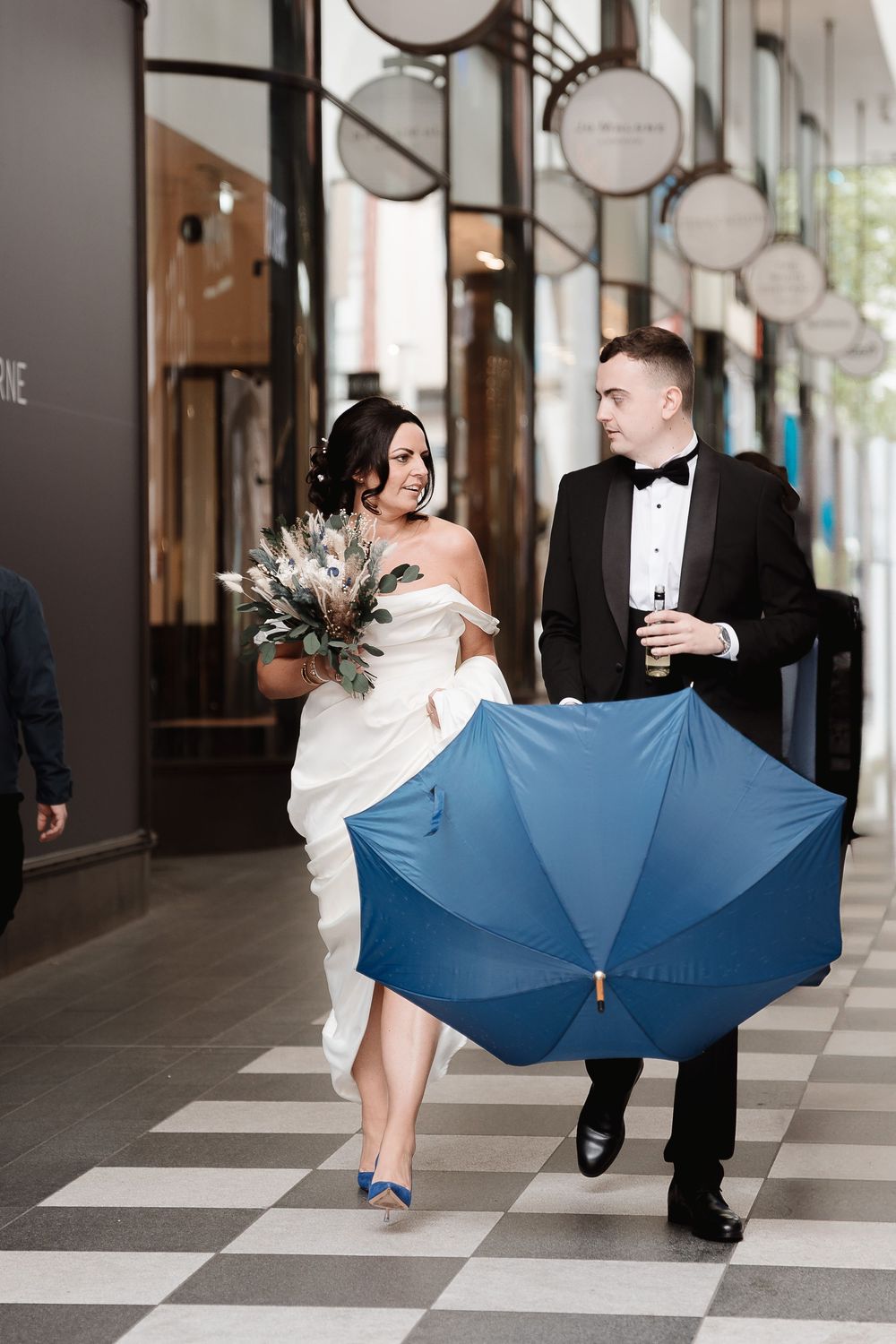 Creative wedding photo series shows couple sharing playful moments with a blue umbrella on a checkered floor.