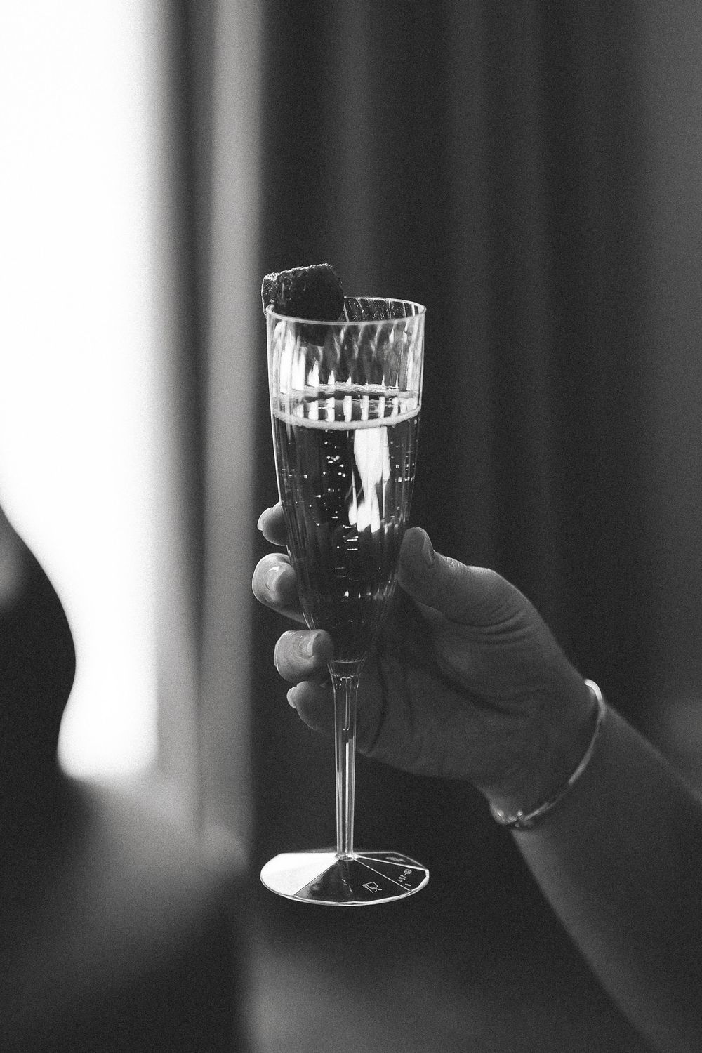 A black and white photo series showing crystal wine glasses being held up in a celebratory toast motion.