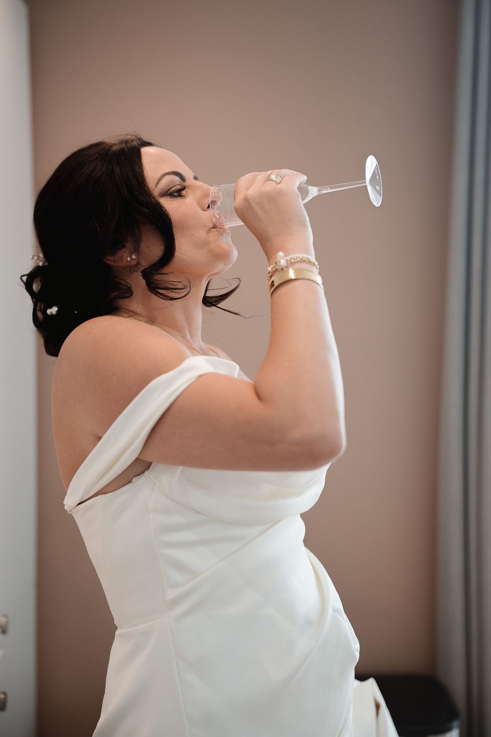 Someone in an elegant white wedding dress takes a sip from a champagne glass during a celebratory moment.