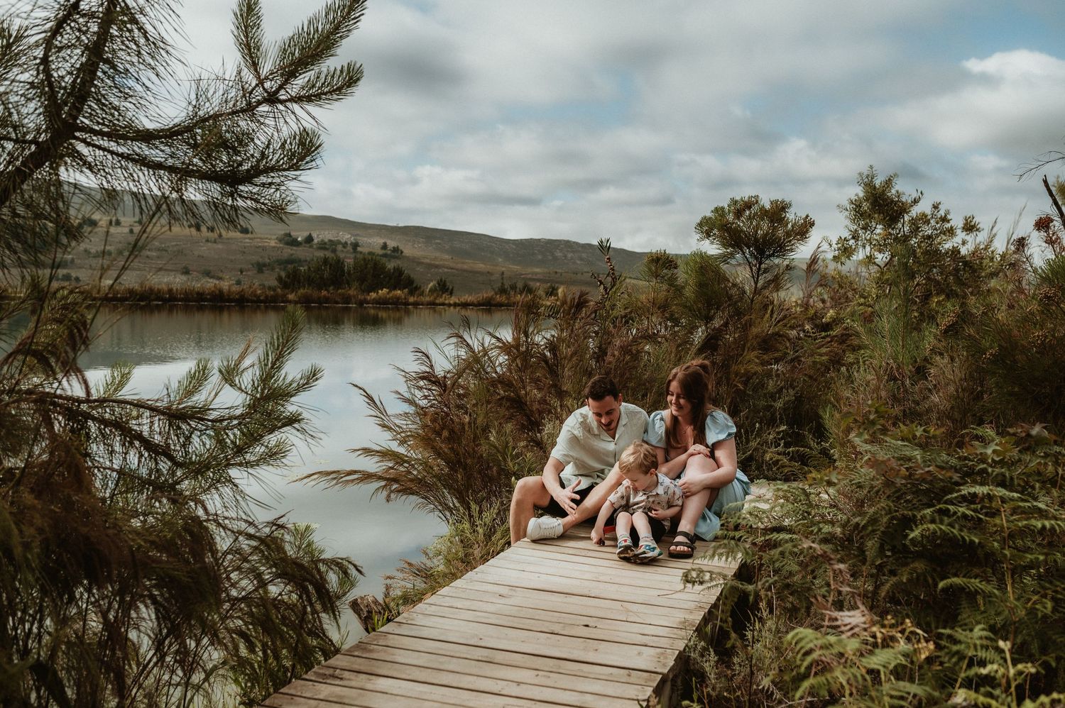 Couple relaxing on wooden boardwalk overlooking serene lake landscape.