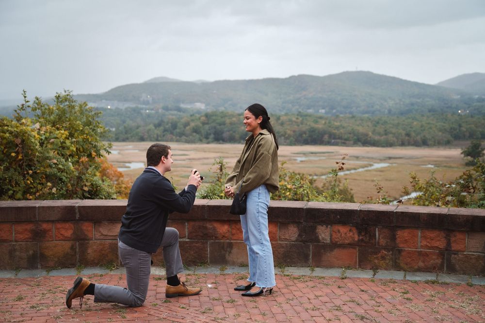 A future groom proposes against a scenic mountain landscape with foliage in the background at Boscobel House & Gardens in Garrison, New York
