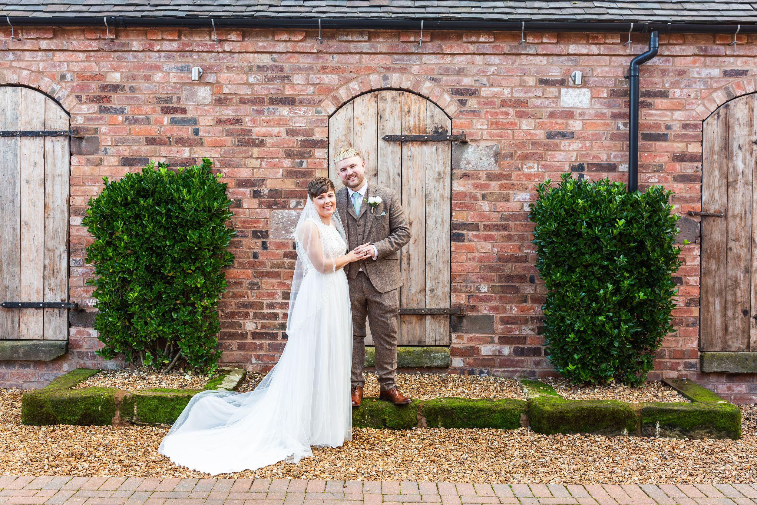Beautiful bridal portrait against rustic brick wall with wooden doors and manicured shrubs at historic venue.