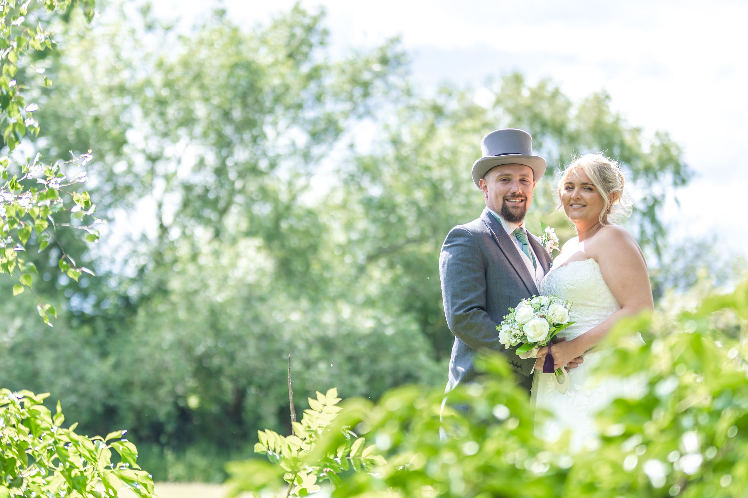A couple shares a romantic moment outdoors among lush greenery during a special celebration.