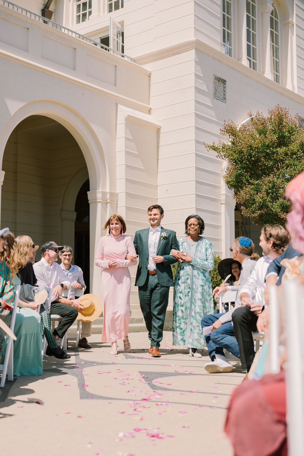 Groom walks hand-in-hand with mother and mother of the bride through cheering guests at Geneva Terrace wedding exit.
