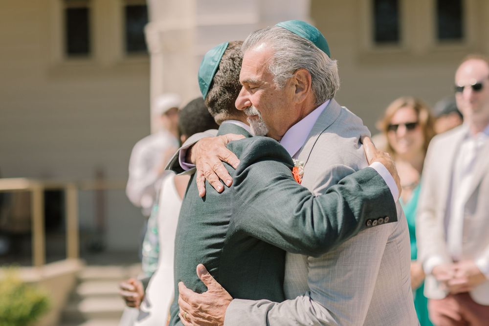 Groom warmly hugs father at the ceremony site at Redlands University’s Geneva Terrace.
