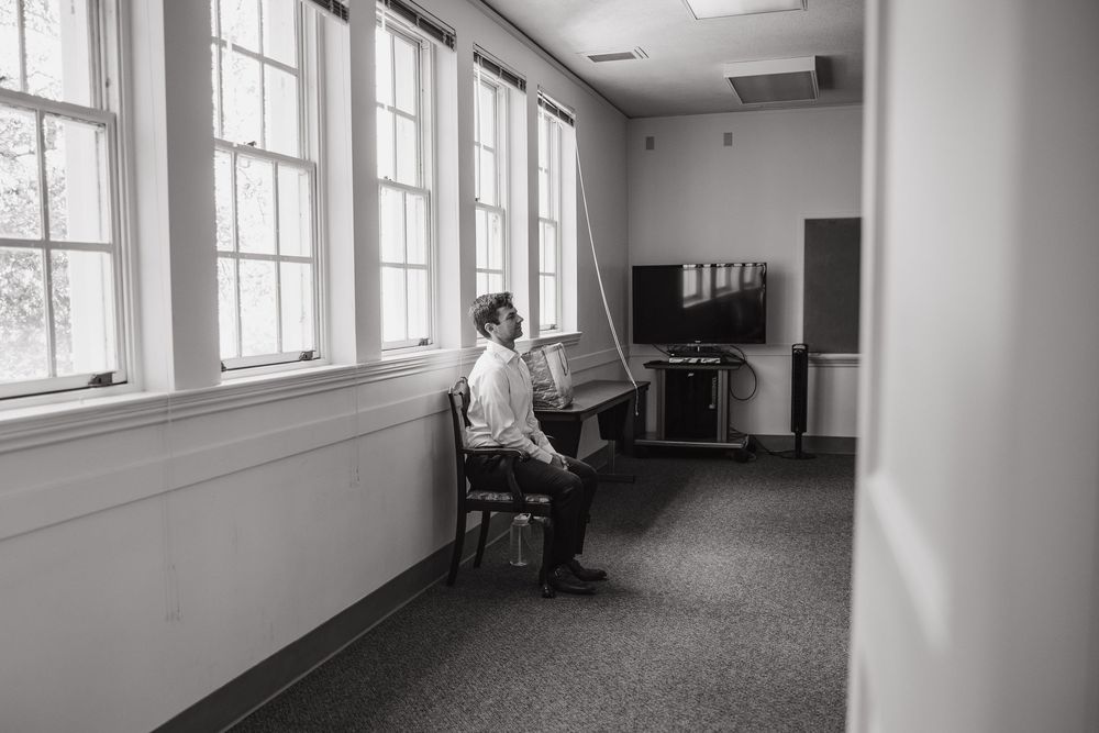 Candid black and white photo of the groom sitting alone in a quiet hallway before the ceremony at Geneva Terrace.