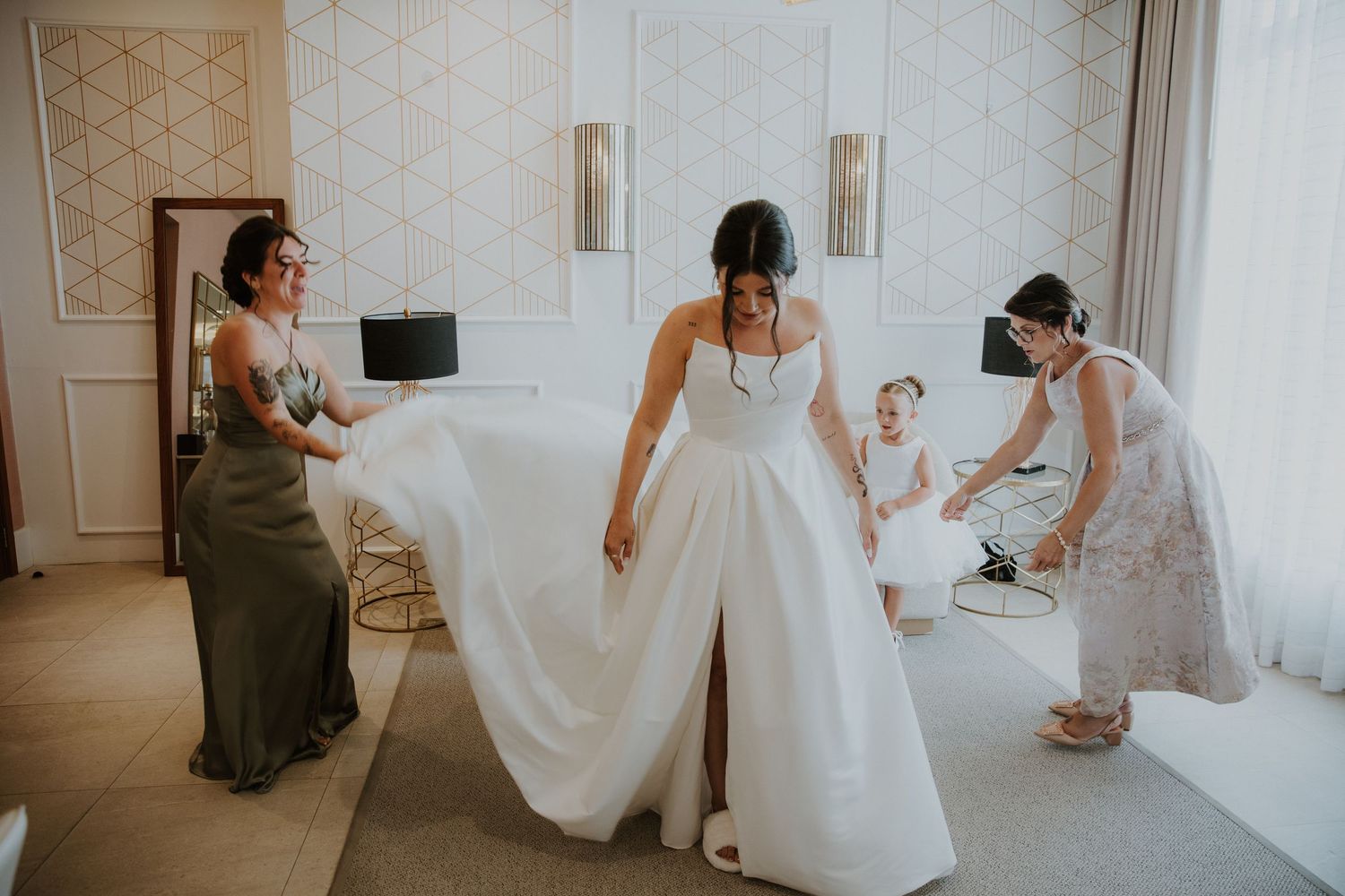 Wedding preparation scene with bride in jumpsuit getting ready with helpers.