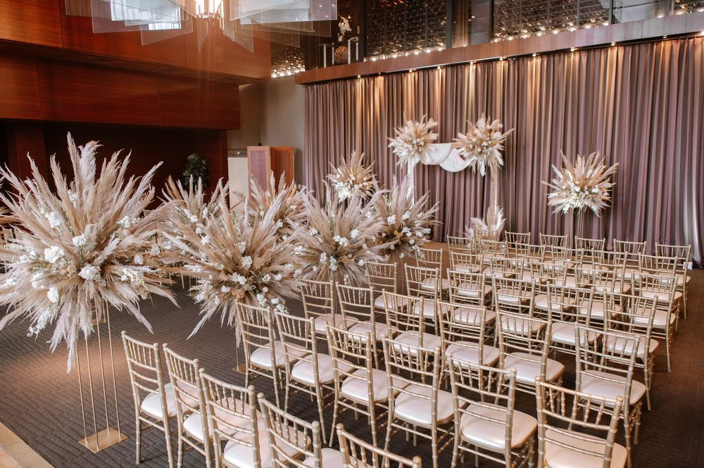 Modern wedding ceremony space with dramatic white starburst chandeliers and gold chiavari chairs arranged in rows.