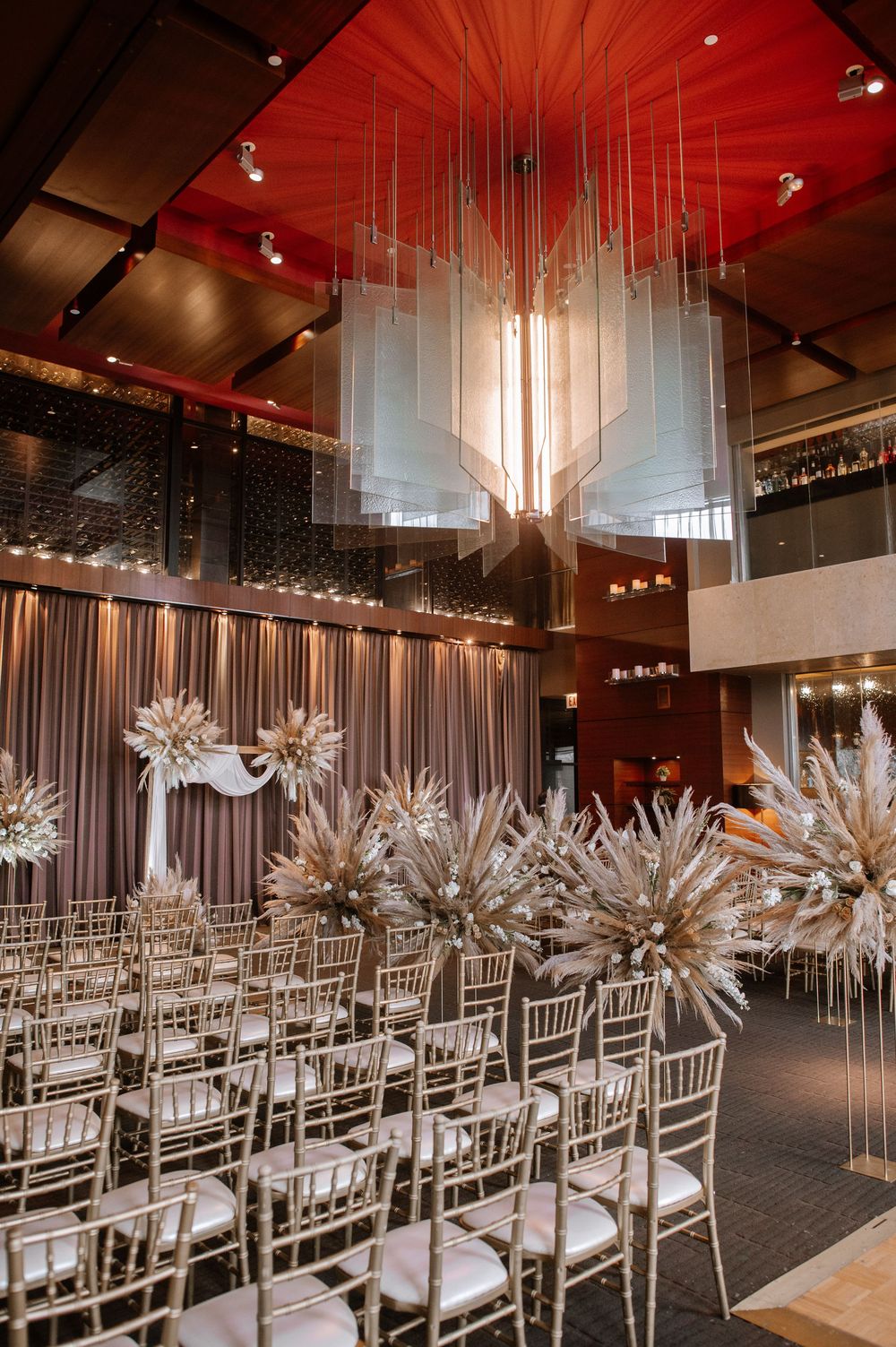 Modern wedding venue with silver chiavari chairs and dramatic white starburst chandelier decorations under red lighting.