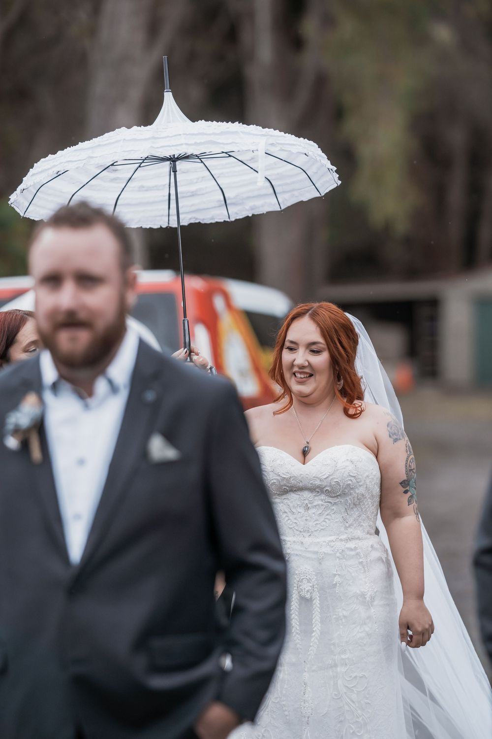 Wedding couple walks together while bride carries a delicate white parasol on overcast day.