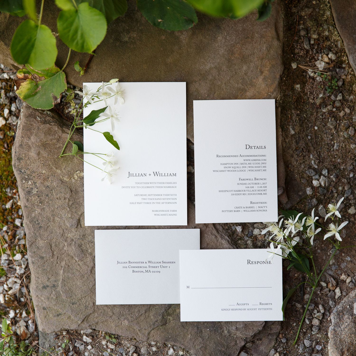 Elegant wedding invitations displayed on a rustic stone wall with green foliage.
