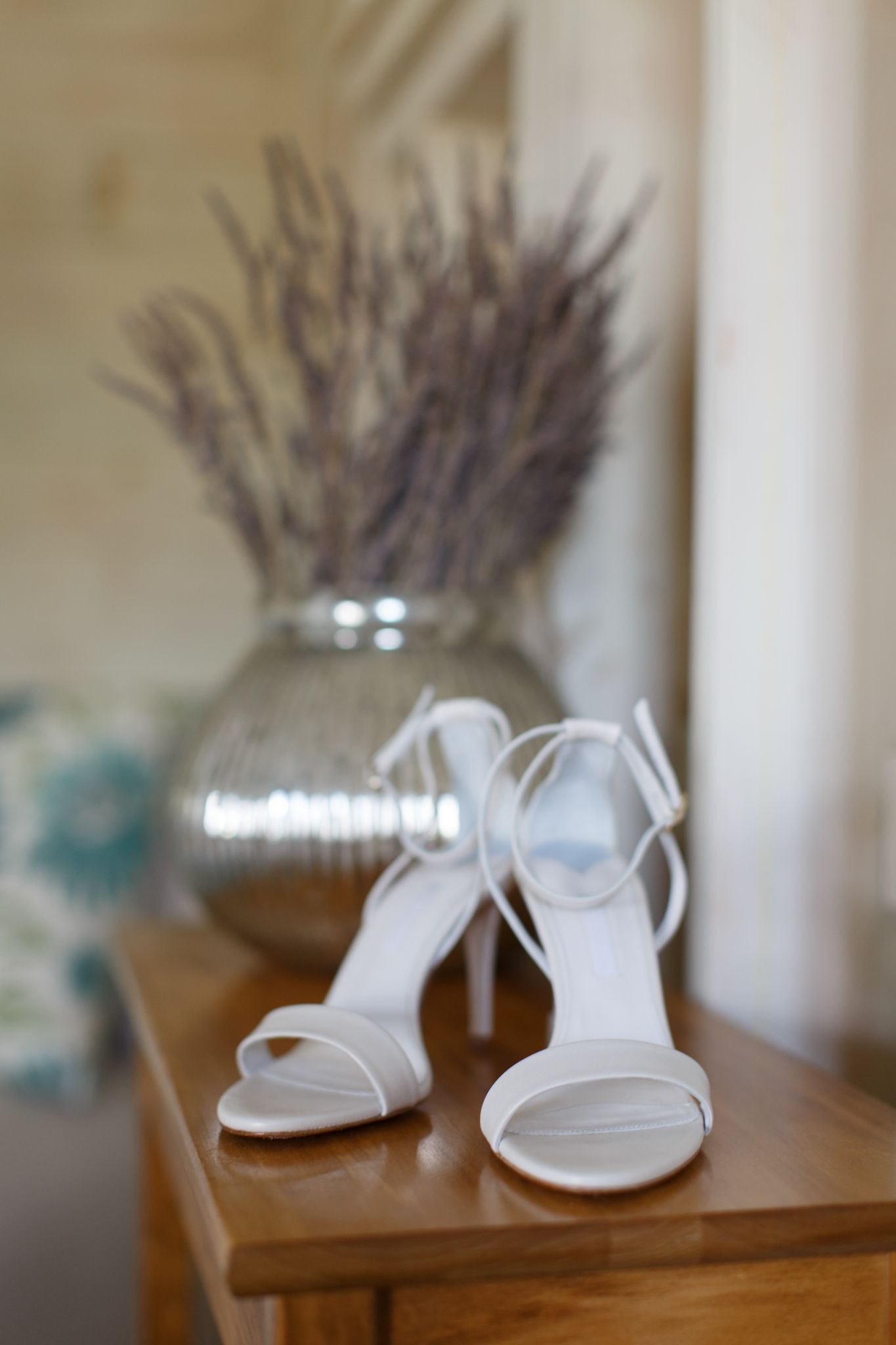 White bridal shoes displayed with dried lavender on a wooden table.