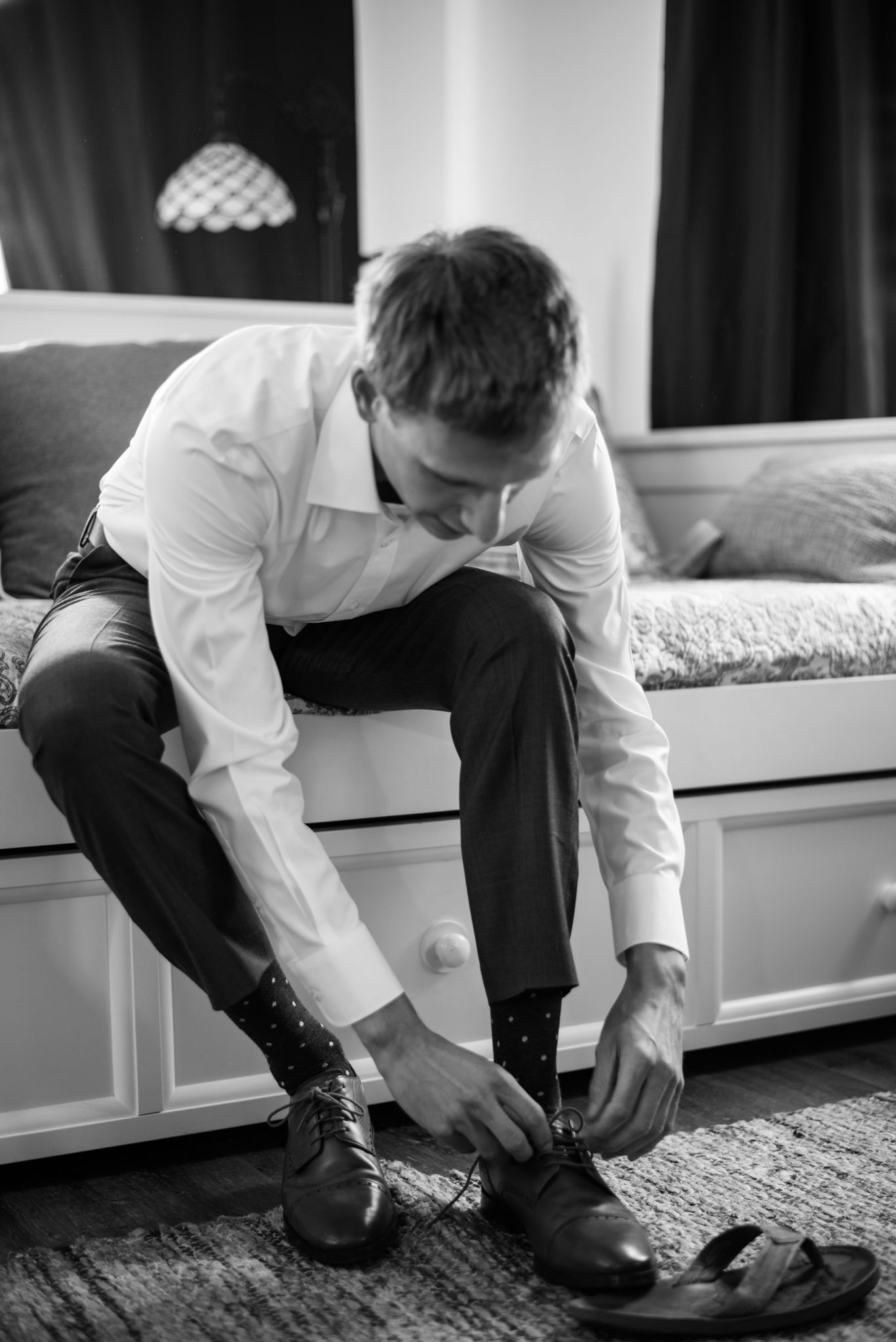 Black and white sequence of someone tying dress shoes while sitting on a white bench.