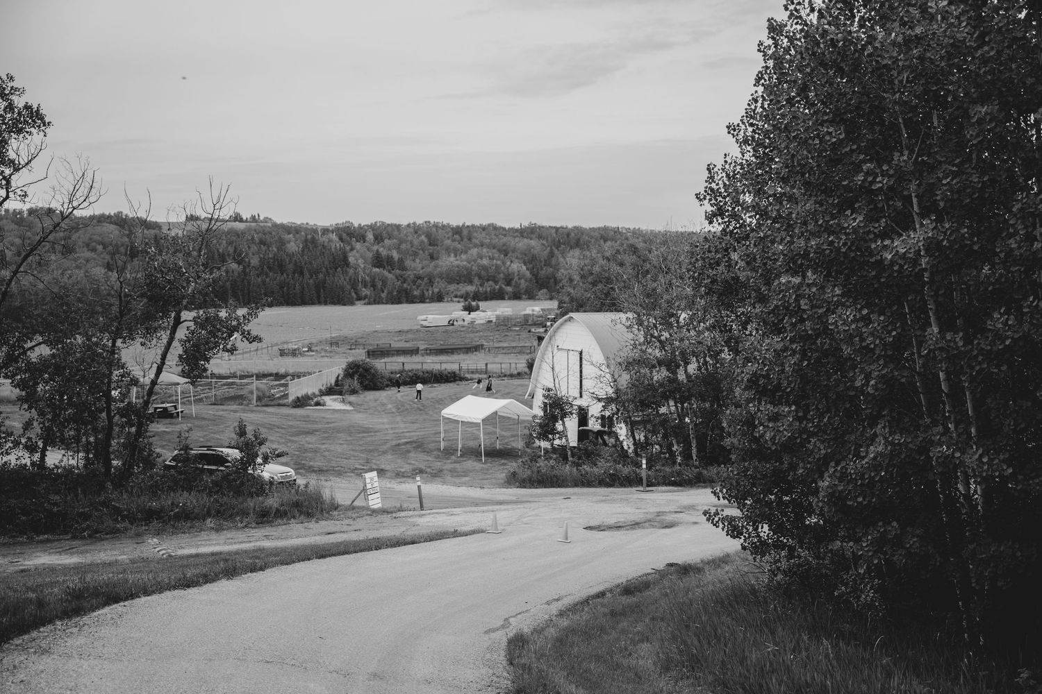 A scenic black and white landscape photo shows a winding rural road cutting through hills and farmland.