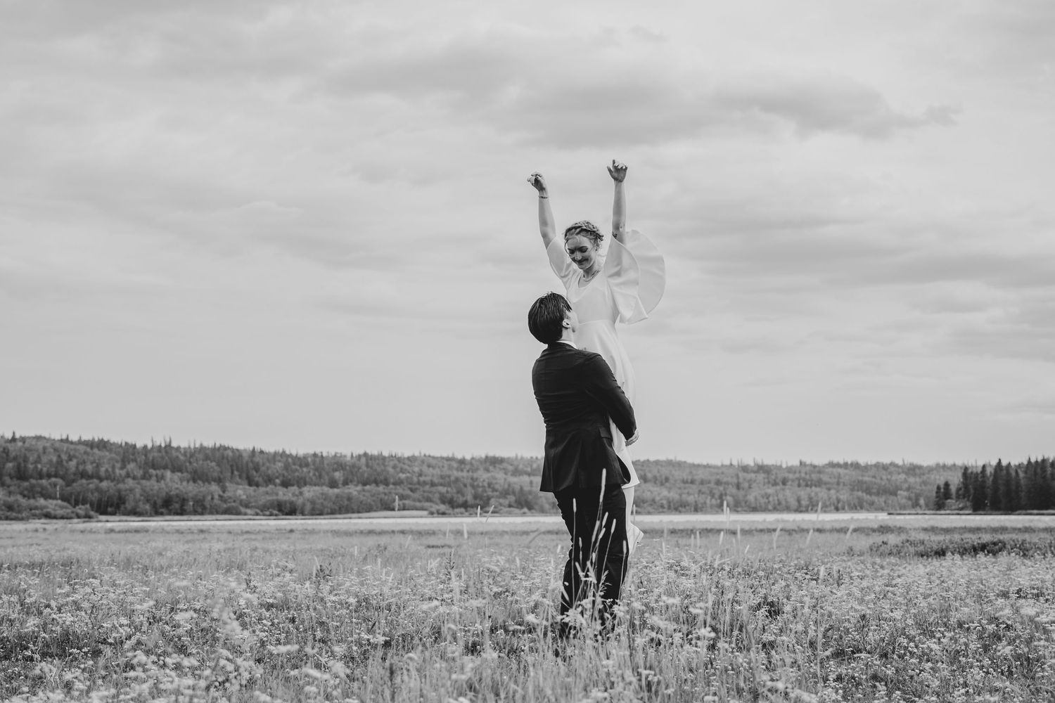 A silhouetted figure stands in an expansive meadow with arms raised to the sky, creating a dramatic black and white scene.
