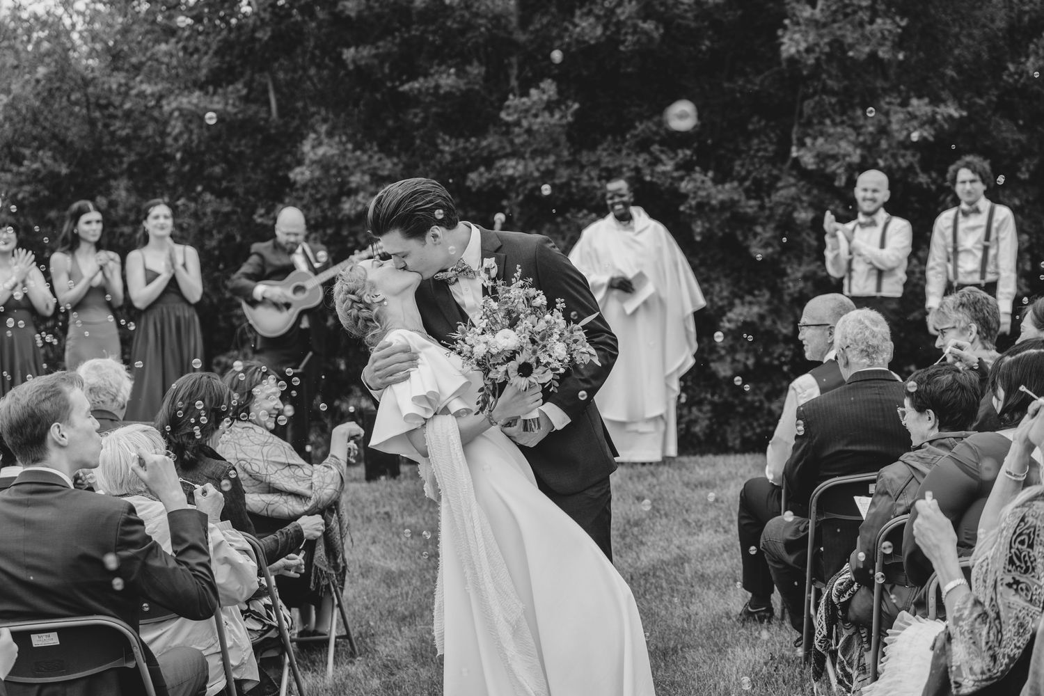 Black and white photo of an outdoor wedding ceremony with guests seated in chairs on a lawn.