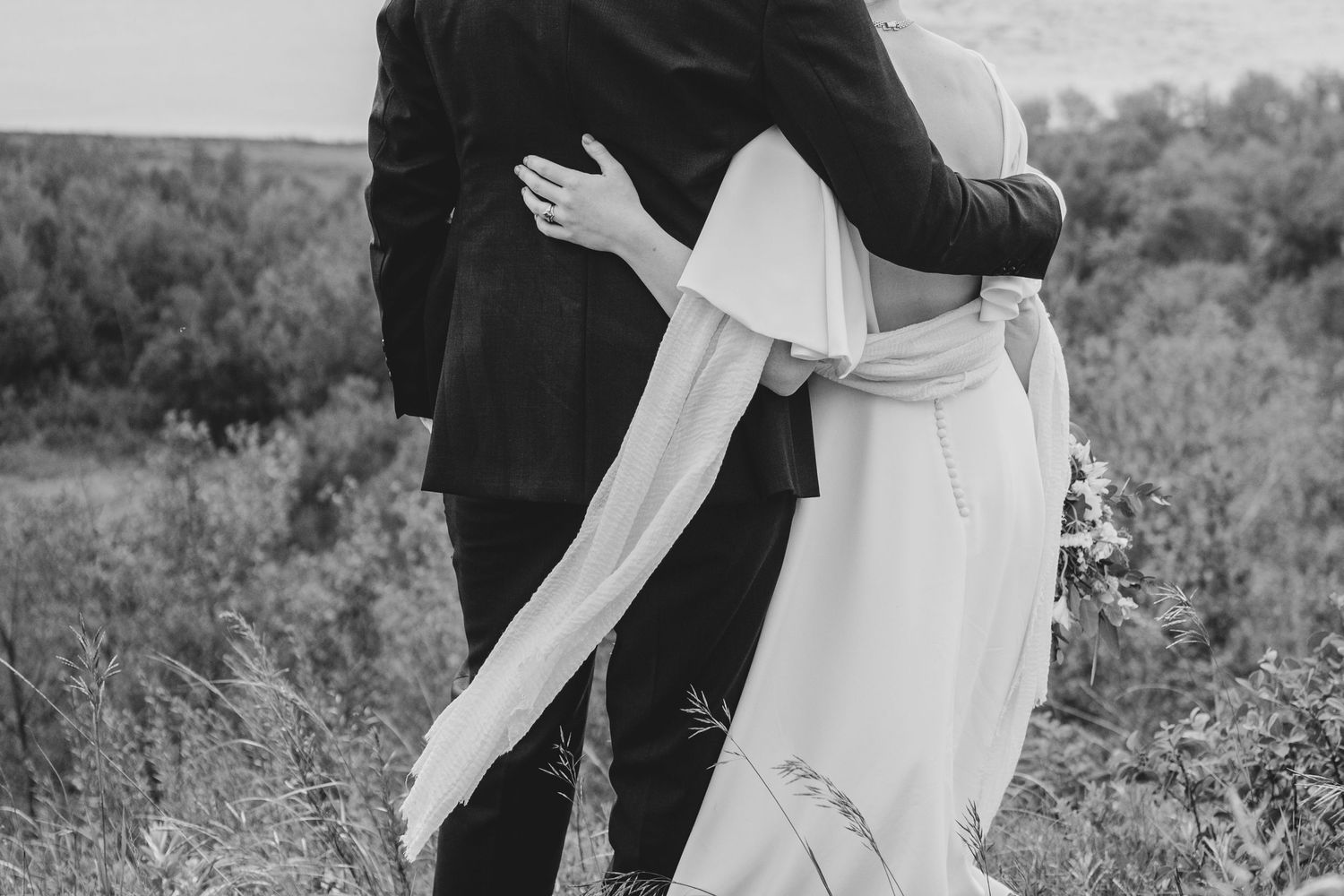A black and white photo capturing an intimate embrace during a wedding celebration.