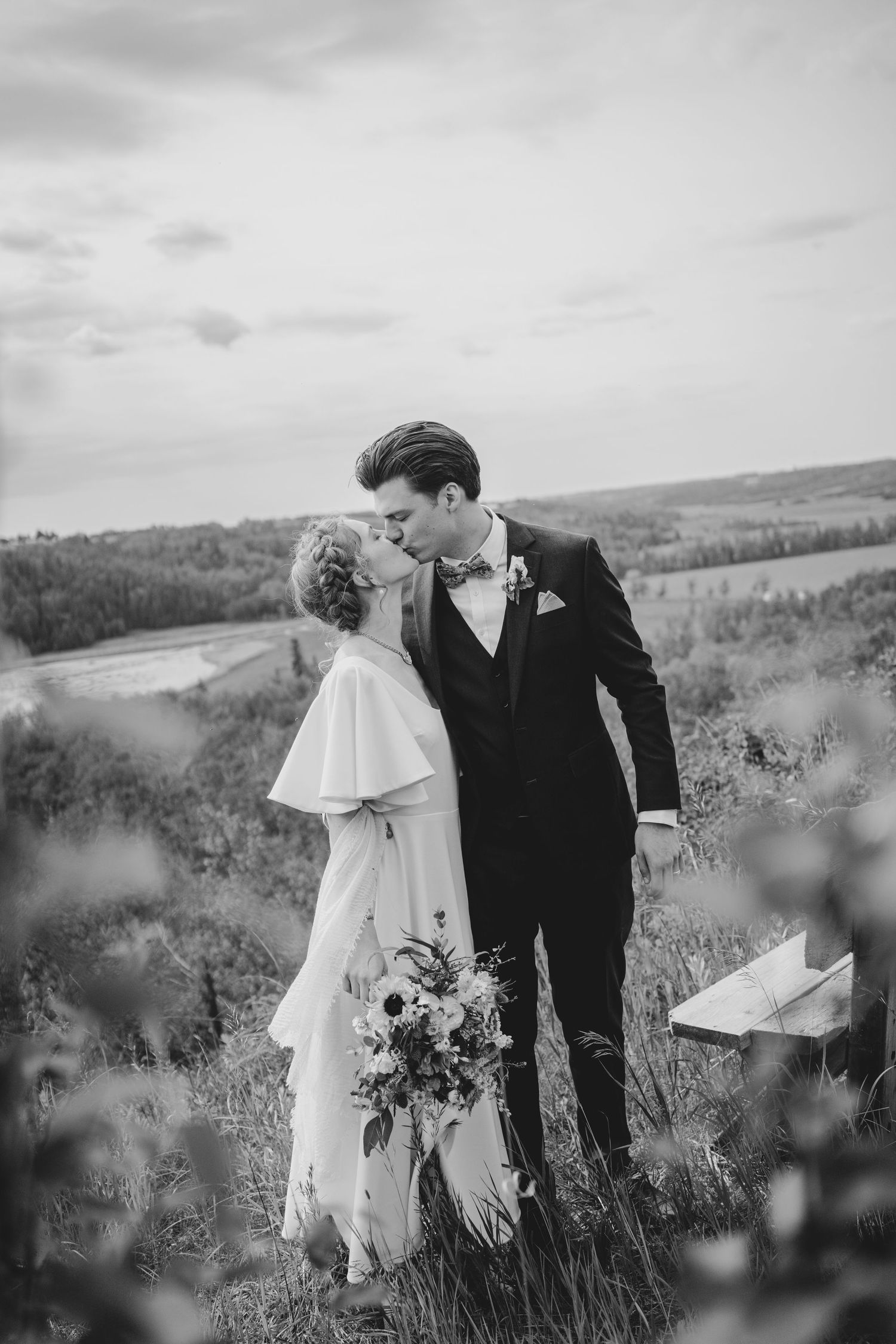 A wedding couple walking through a scenic mountain meadow shown in black and white.