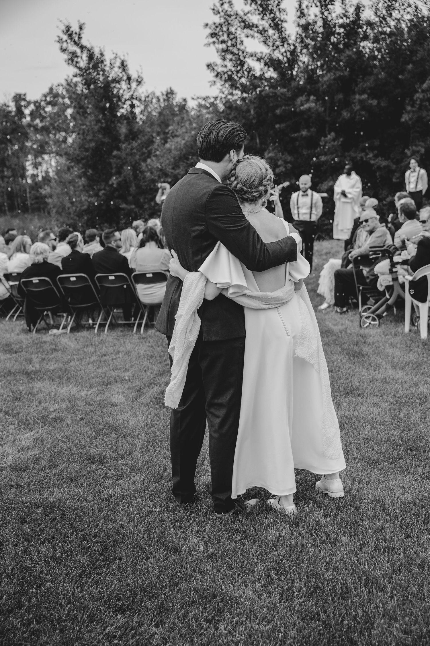 A tender moment captured in black and white at an outdoor wedding with folding chairs and guests.