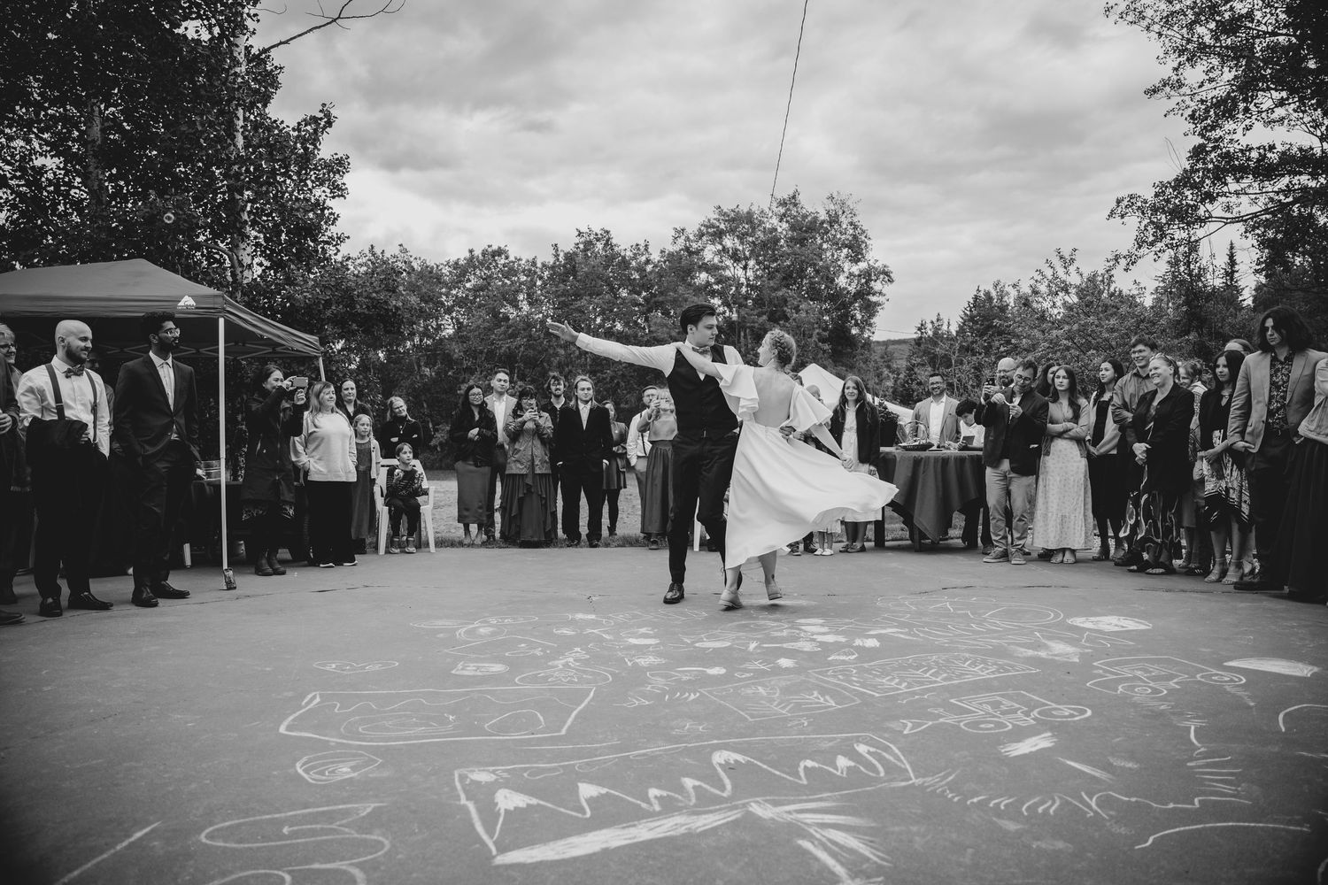 A black and white wedding photo showing dancing on an outdoor dance floor with chalk drawings.