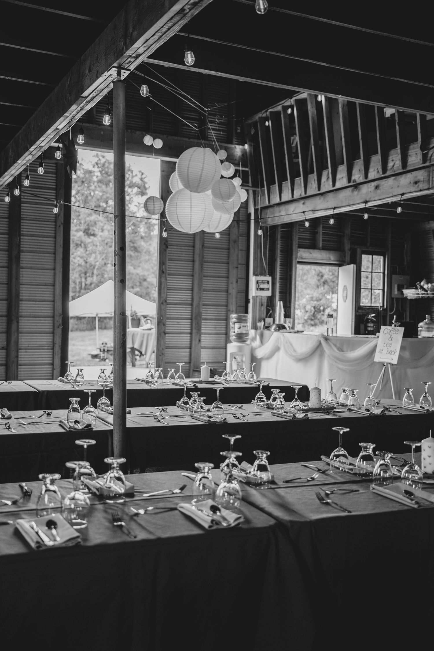 Black and white panoramic view of a dimly lit banquet hall set up with tables adorned with white decor and paper lanterns.