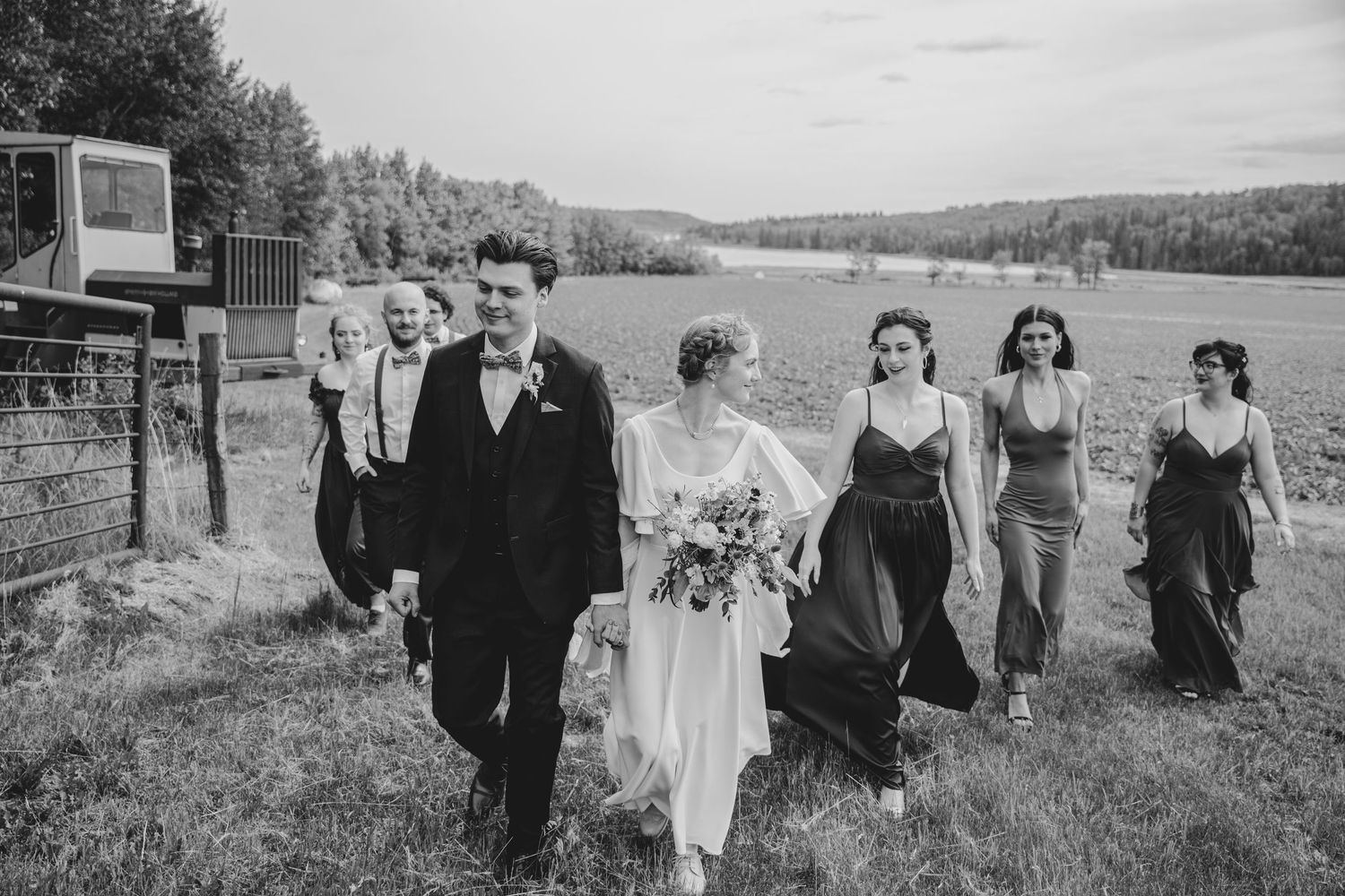 A wedding party walks through a scenic field surrounded by mountains in black and white.