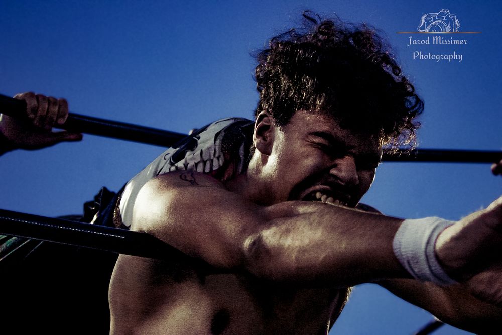 Professional wrestler grimaces while locked in submission hold during intense match.